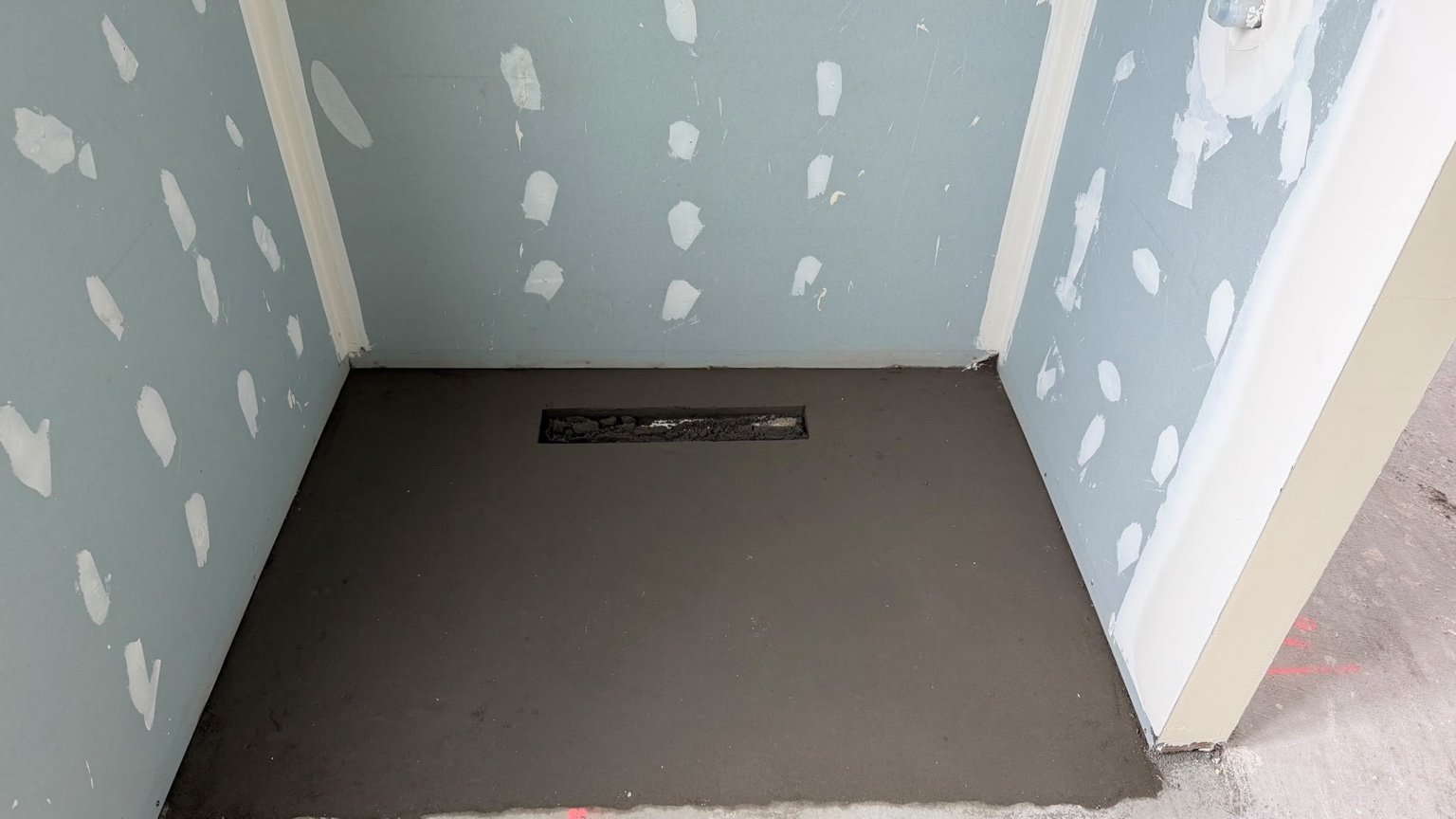 Client shower floor screed prepared around a linear drain before waterproofing and tiling